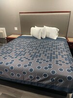 A hotel room with a bed featuring a geometric patterned bedspread, a wooden headboard, and two white pillows.