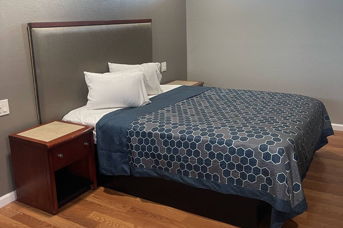A bedroom with a bed, wooden nightstand, and a window.