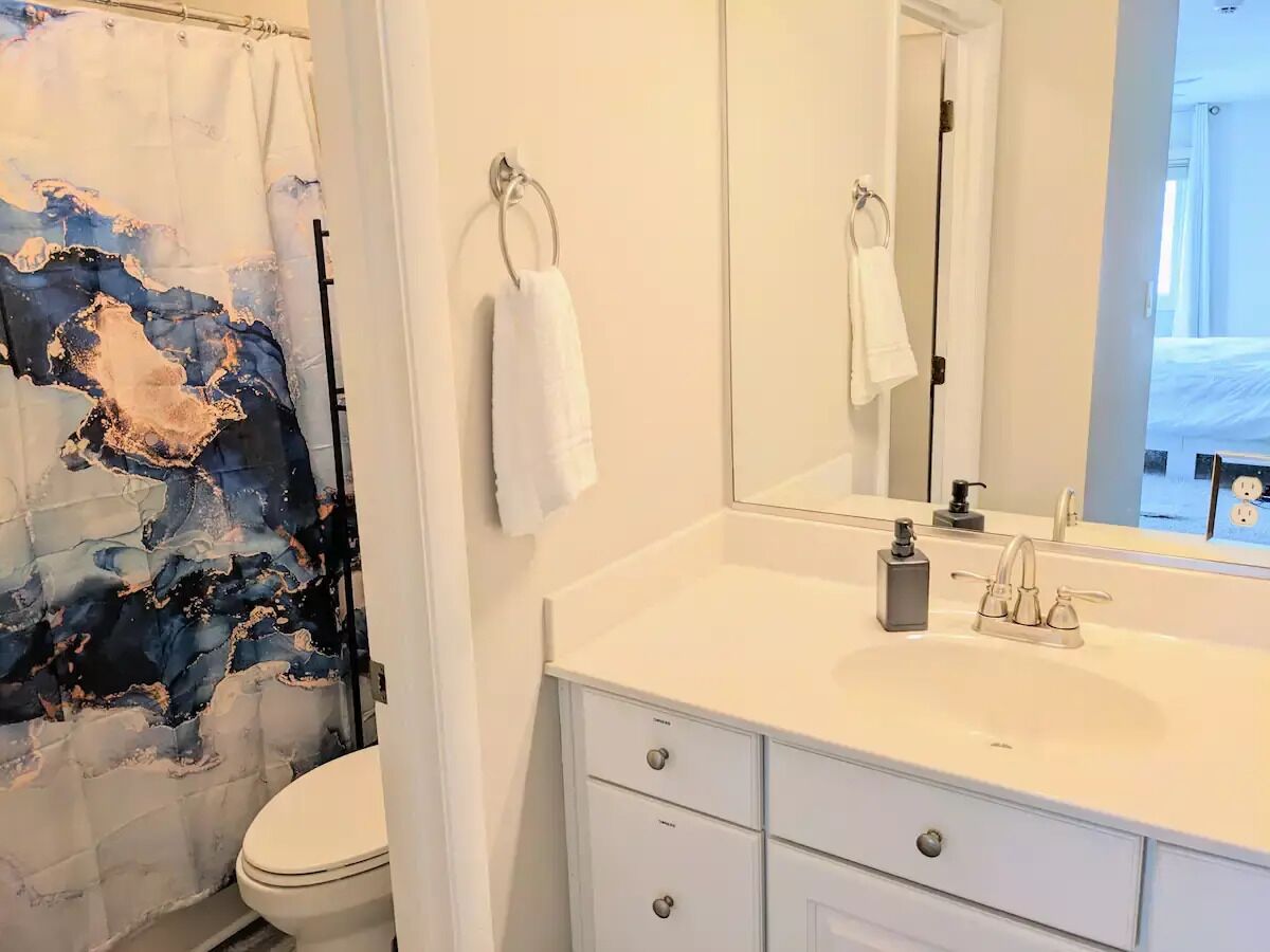Un baño con un lavamanos blanco, un espejo y una cortina de ducha con un diseño abstracto azul y blanco.