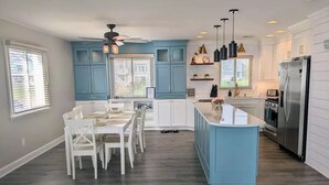 A modern kitchen with blue cabinets, a central island, and a dining area with white chairs.