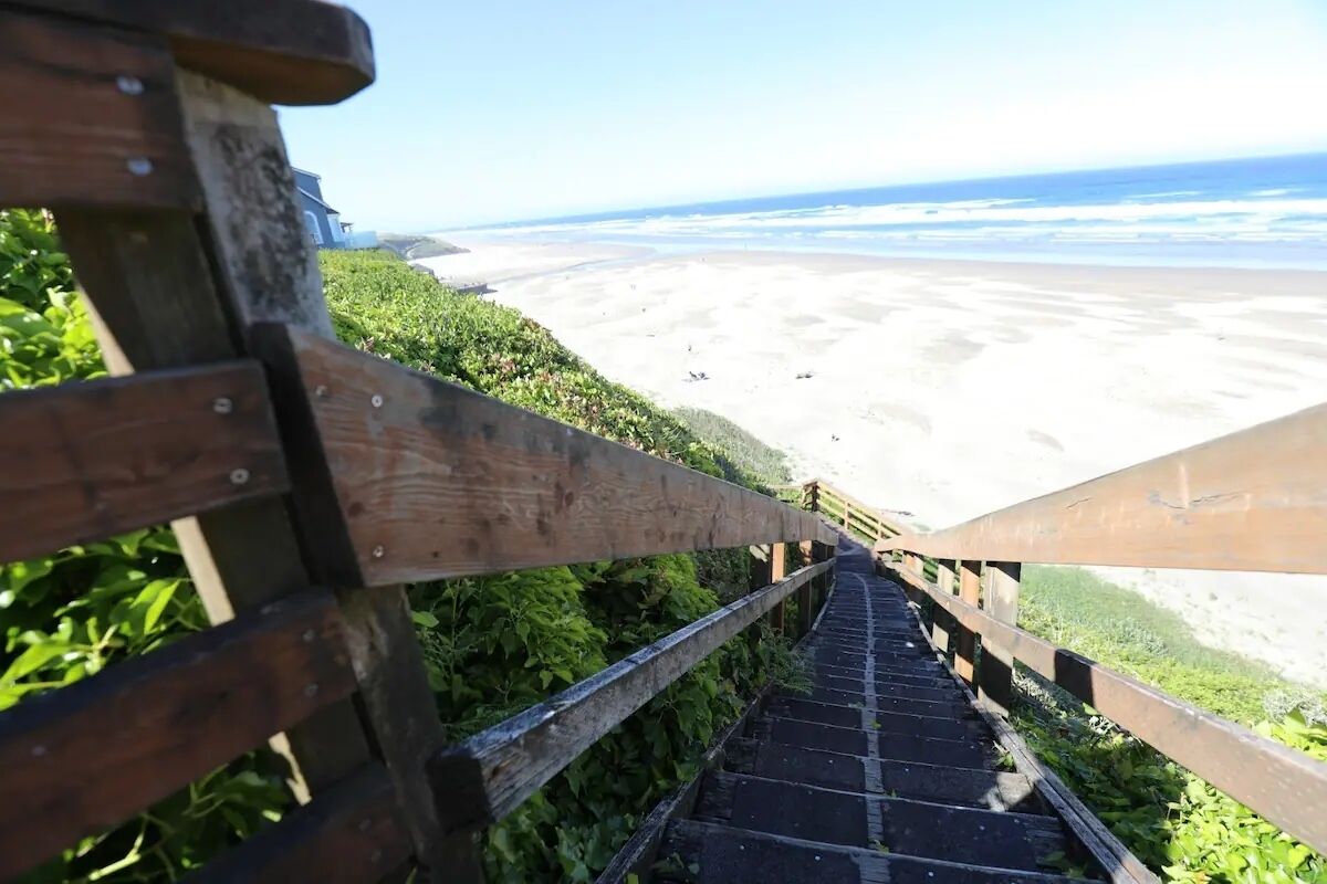 A wooden staircase leading to a beach with a clear view of the ocean.