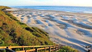 Un paysage côtier avec une plage de sable, une clôture en bois et une colline herbeuse.
