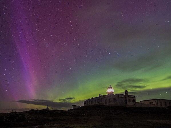 A building with a dome, under a night sky with visible stars and the aurora borealis.