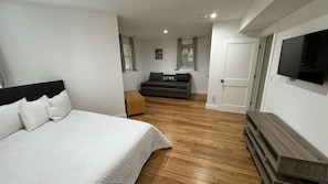 Une chambre à coucher avec un lit, un canapé, une télévision et un plancher en bois.
