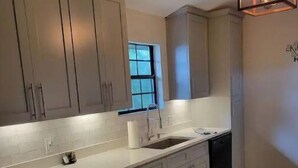 Une cuisine avec des meubles de couleur gris clair, un plan de travail blanc, un lave-vaisselle encastré et une fenêtre avec vue.