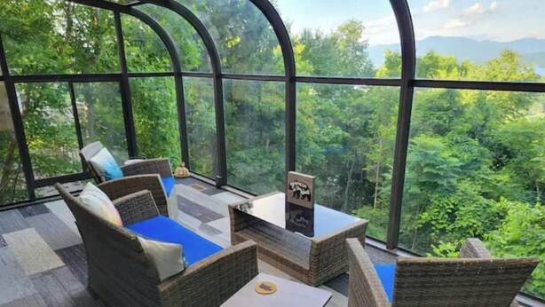Une pièce chaleureuse, meublée de mobilier en osier, avec une petite table et une vue sur une végétation luxuriante, visible à travers de grandes fenêtres.