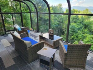 Una habitación acogedora con mobiliario de mimbre, una pequeña mesa y vistas a exuberante vegetación a través de amplias ventanas.