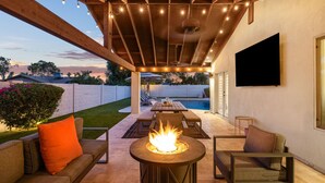 Eine Außenpatio mit Feuerstelle, Sitzgelegenheiten und einem an der Wand befestigten Fernseher.