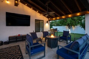 An outdoor patio with a fire pit, seating, a TV, and a grill.