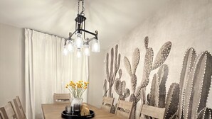 Ein Esszimmer mit Holztisch und Stühlen, einer Kristalllüster und einer Wandmalerei mit Kakteenmotiven.