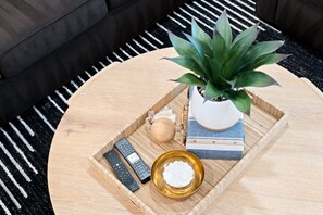 A round wooden tray on a coffee table with a potted plant, a remote control, a small bowl, and a book.