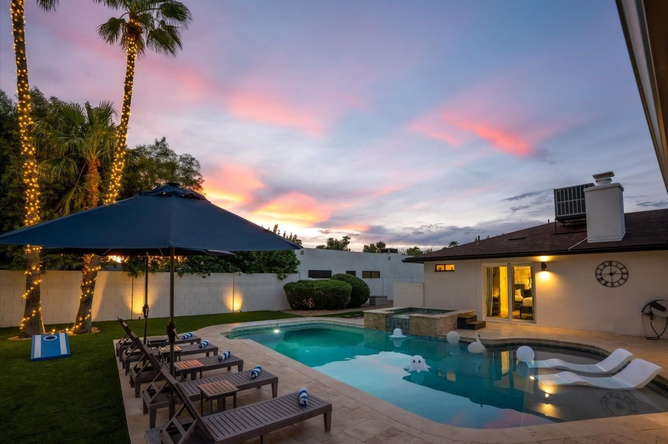 Dusk view of the private pool, hot tub, and synthetic grass lawn lit by ambient backyard lights.