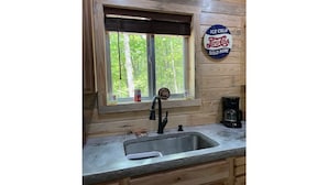 A kitchen with a window, a sink, a coffee maker, and a sign indicating 'Ice Cold Pepsi' is sold. - Nostalgic Route 66 Cabin with Meramec River Access (Bourbon)