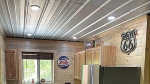 A kitchen with wooden cabinets, a stainless steel refrigerator, a window with a view, and a Route 66 sign on the wall. - Nostalgic Route 66 Cabin with Meramec River Access (Bourbon)