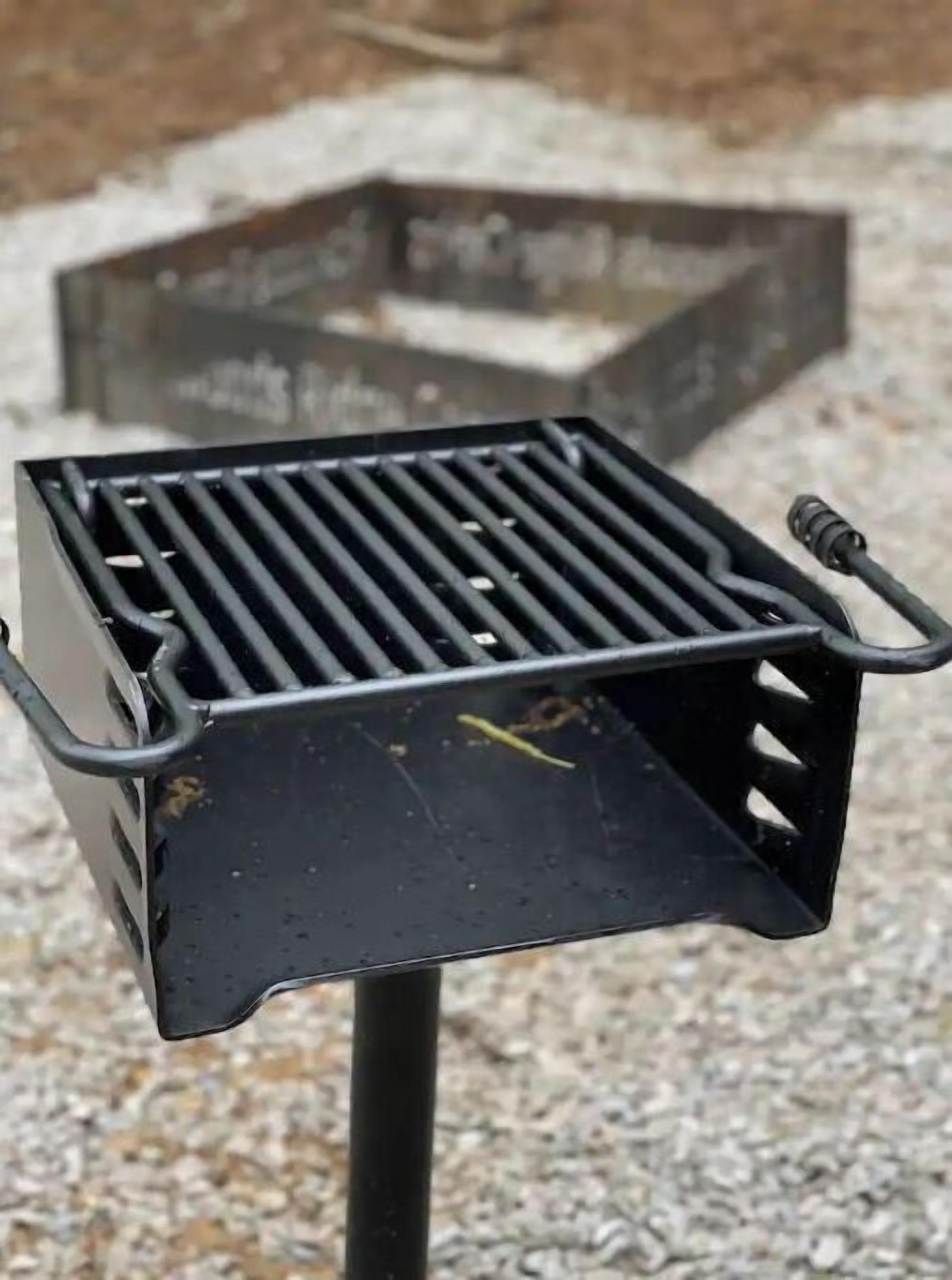 A black metal grill with a handle, placed on a gravel surface.