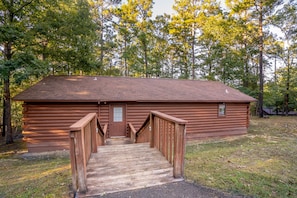 A log cabin with a wooden staircase leading to a door, surrounded by trees.
