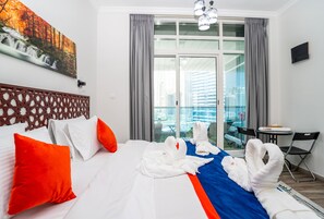 Quarto de hotel com cama, vista da cidade através de grandes janelas, área de refeições e um quadro na parede.