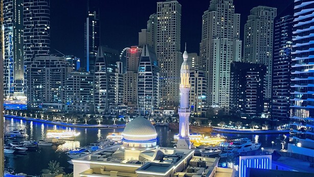 A cityscape with modern high-rise buildings, a mosque with a prominent minaret, and a waterfront area with boats and a bridge. - ZAPBED House OPT 701&34 (Dubai)