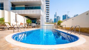 A swimming pool with lounge chairs and umbrellas, surrounded by a modern building with a city skyline in the background. - ZAPBED House OPT 701&34 (Dubai)