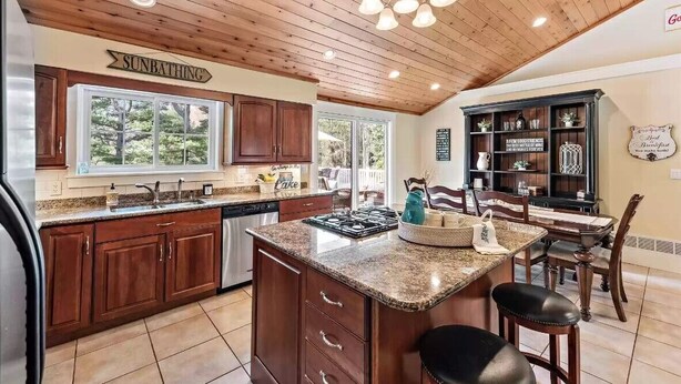 A kitchen with wooden cabinets, a granite countertop island, and a dining area with a table and chairs. - Perfect retreat for multi-generational families! Sat-Saturday lakeside rental. (Three Oaks)