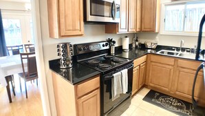 Una cucina con mobili in legno, piano cottura in acciaio inossidabile, forno a microonde e piano di lavoro nero.