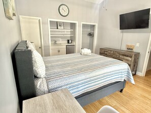 A bedroom with a bed, bedside tables, a wardrobe, a television, and a clock on the wall.