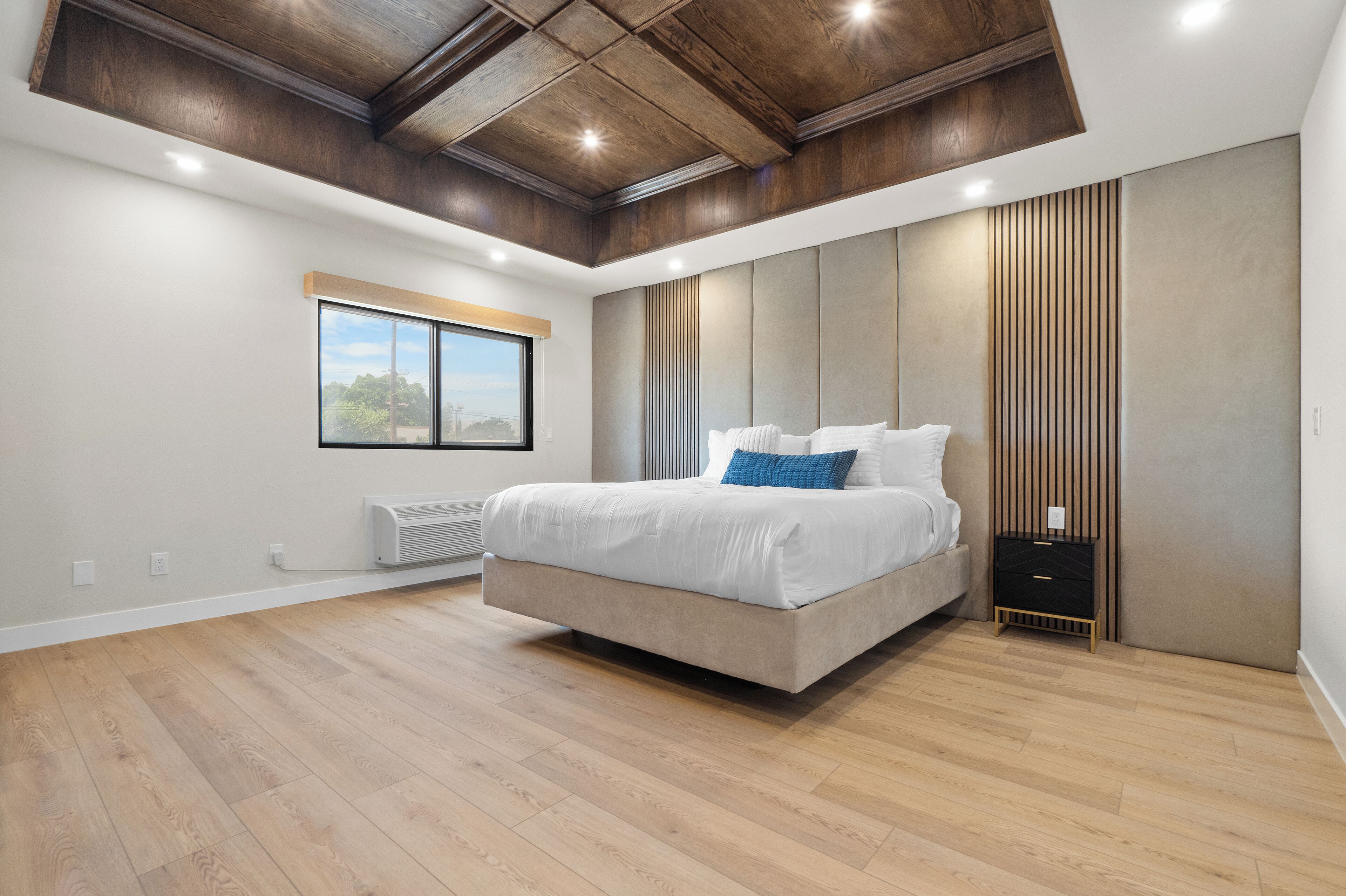 A modern bedroom with a large bed, wooden ceiling, and a window.
