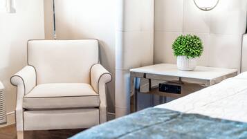 A modern bedroom with a bed, a chair, a bedside table with a plant, and a wall-mounted light fixture.