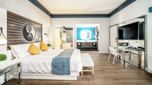 A modern hotel room with a large bed, a desk, and a TV. - Aspire Inn Studios & Spas (Bellflower)