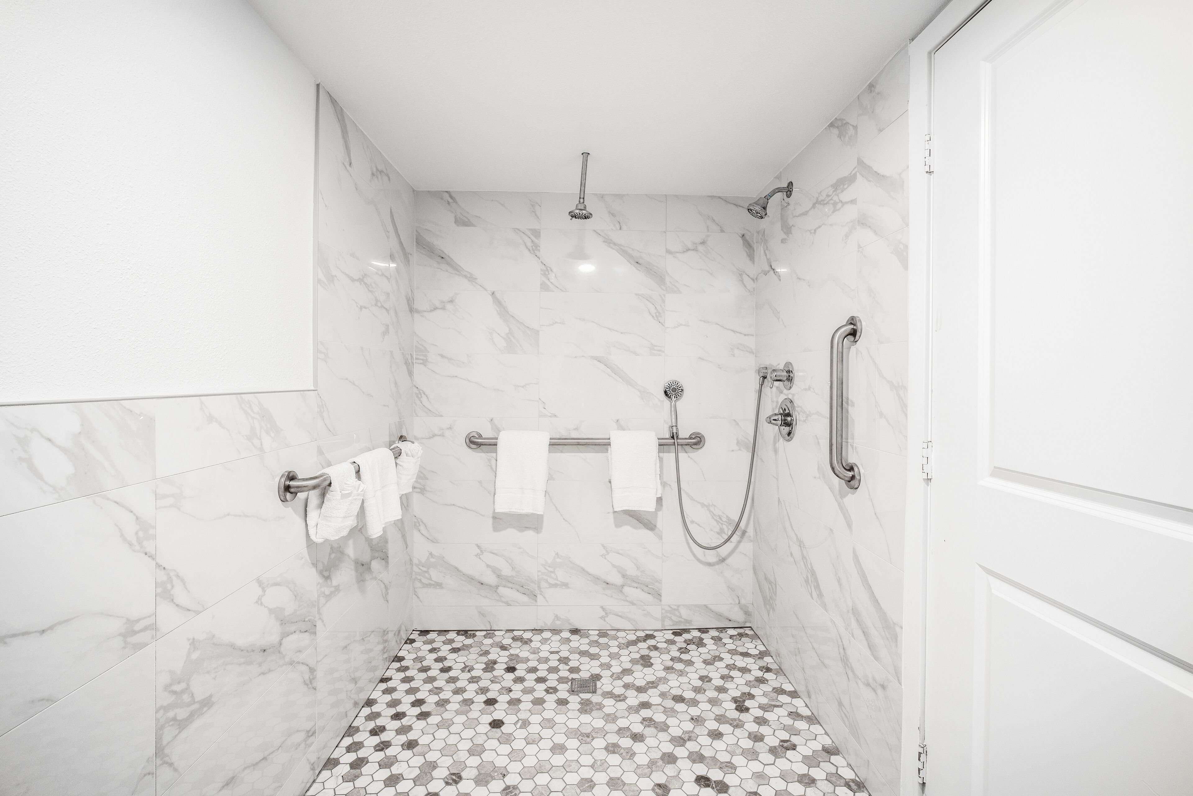 A modern bathroom with marble walls, a shower with a handheld showerhead, and a tiled floor.