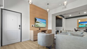 A modern living room with a wooden accent wall, a flat-screen TV, a grey sofa, and a coffee table. - Aspire Inn Studios & Spas (Bellflower)