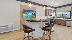 A modern kitchen with a central island, bar stools, and a large TV displaying a tropical scene. - Aspire Inn Studios & Spas (Bellflower)