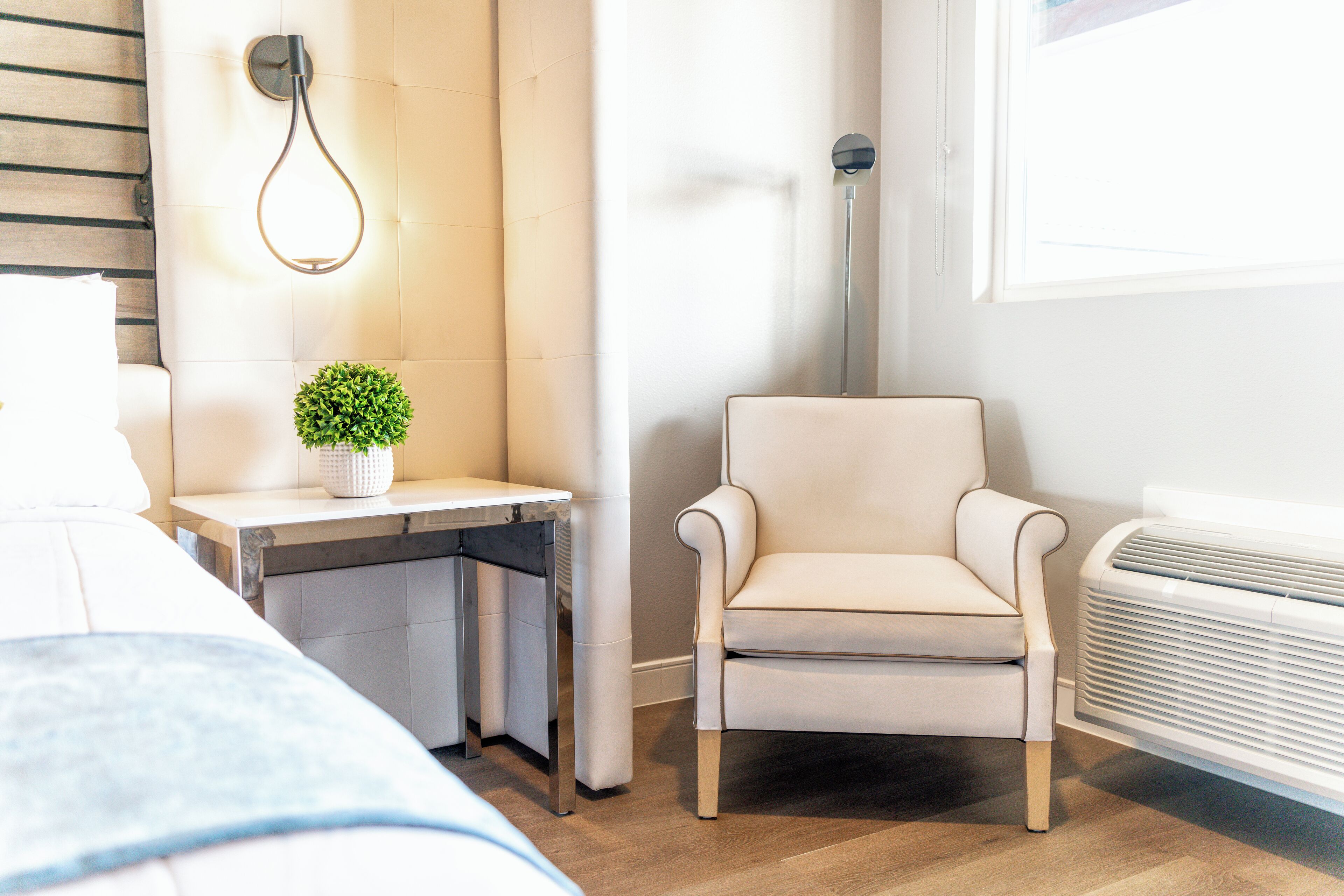 Une chambre d’hôtel moderne équipée d’un lit, d’un petit bureau avec une plante, d’une chaise et d’un radiateur portatif.