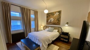 A bedroom with a bed, bedside tables, a bench, a TV, and a painting on the wall. - Peaceful full home in the heart of Southside Flats. (Pittsburgh)