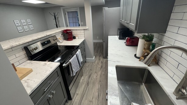 A modern kitchen with a stove, oven, and sink. There is a window with curtains and a refrigerator.