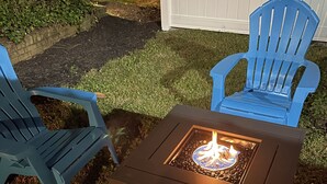 A fire pit table with two blue Adirondack chairs.