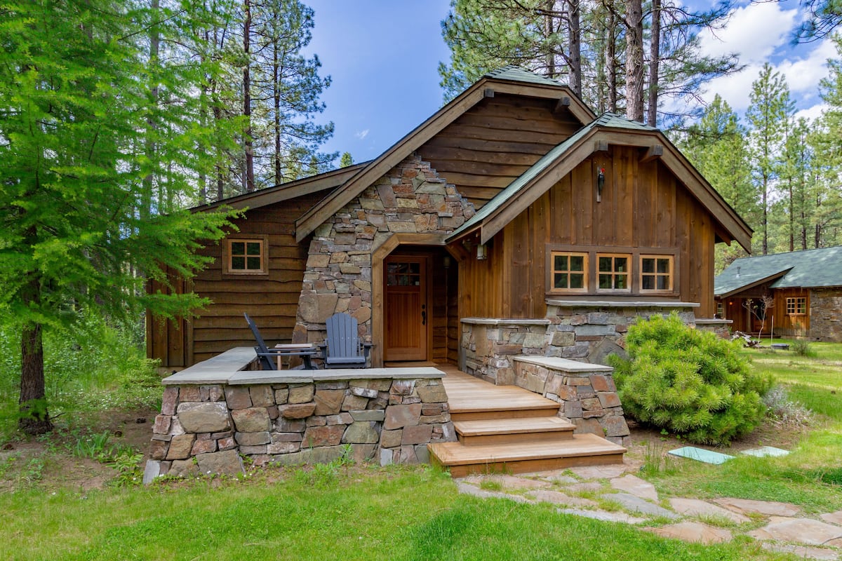 A log cabin with a stone foundation, wooden exterior, and a front porch with a bench and table.