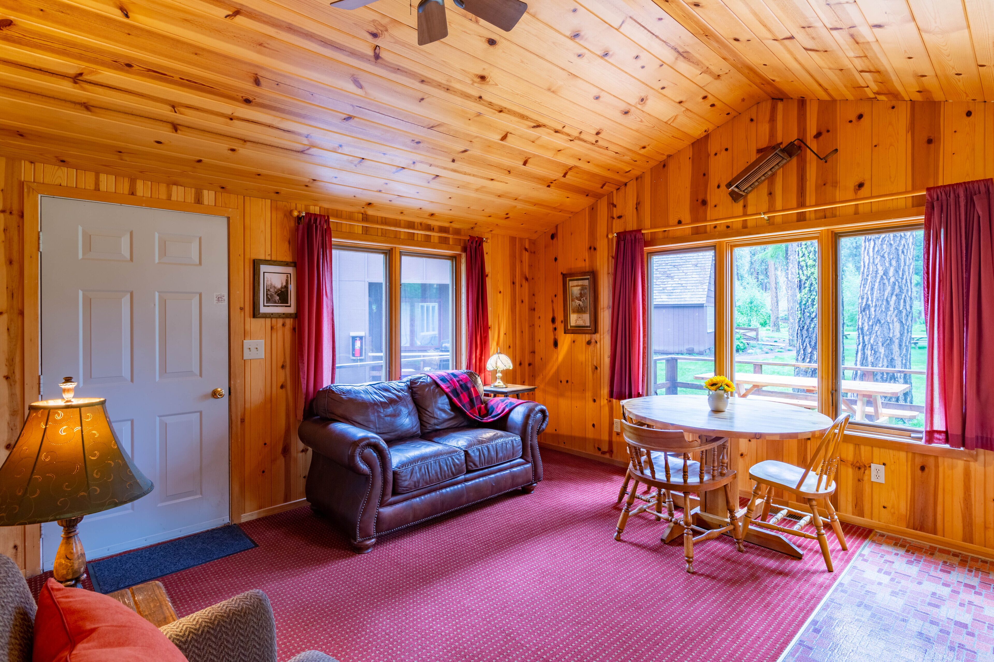 Een houten cabin met een leren bank, een eettafel met stoelen en grote ramen voorzien van gordijnen.