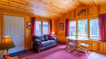 Een houten cabin met een leren bank, een eettafel met stoelen en grote ramen voorzien van gordijnen.