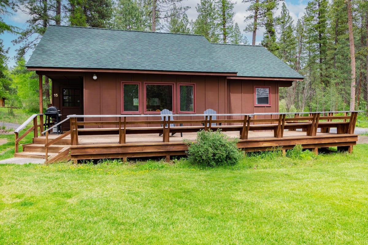 A cabin with a wooden deck and a covered porch, surrounded by a forest.