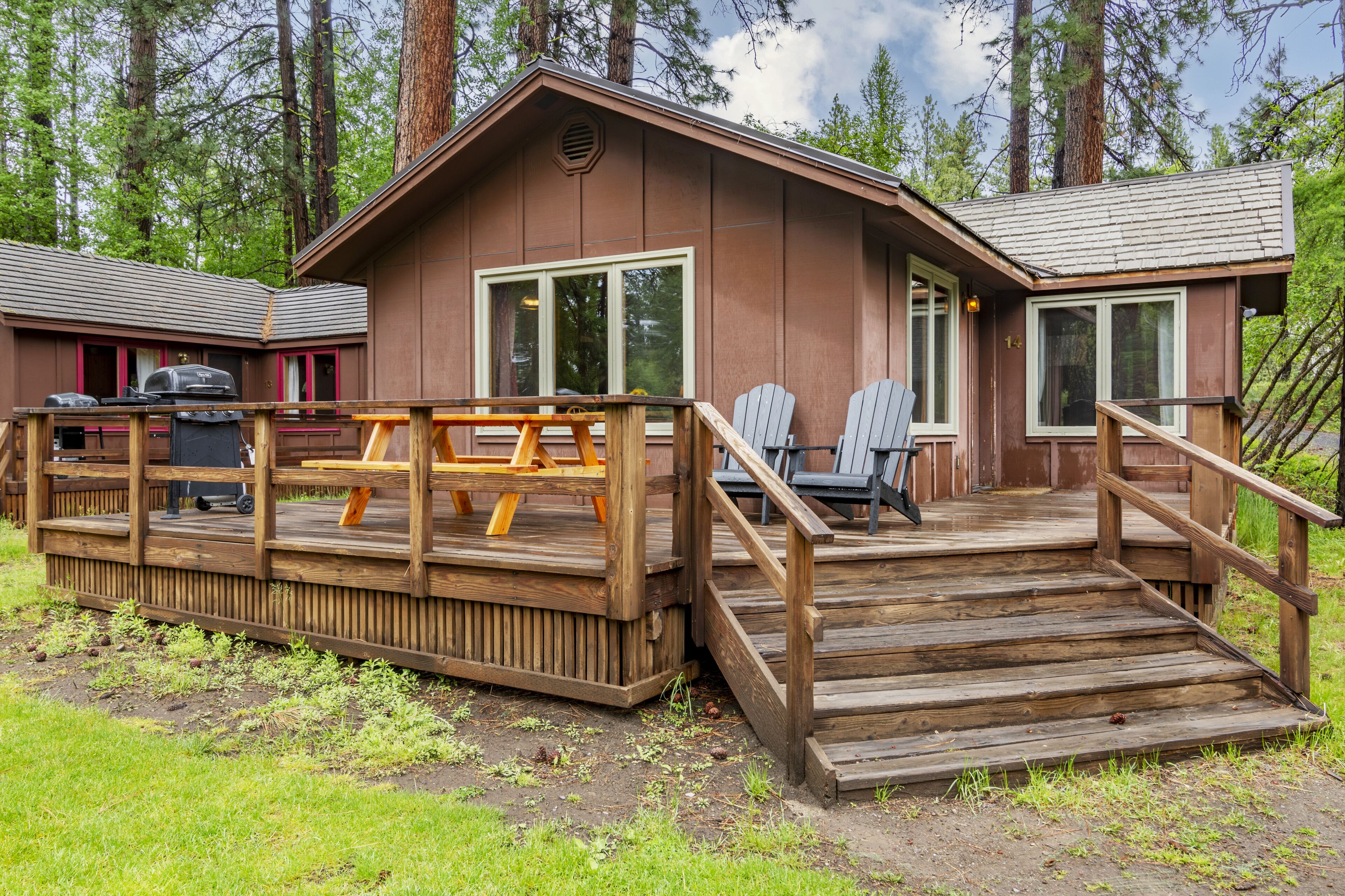 A cabin with a wooden deck, outdoor seating, and a grill.