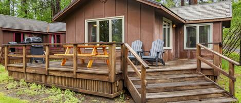 A cabin with a wooden deck, outdoor seating, and a grill.