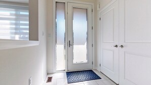 En hall med en vit dörr, en blå matta och ett fönster med persienner.