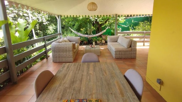 Una veranda esterna con mobili in vimini, un'amaca e un tavolo di legno.
