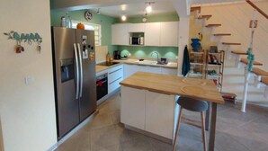Una cucina compatta con frigorifero, microonde e lavello. Un'isola in legno con una sedia. La cucina presenta mobili bianchi e una parete verde decorativa.