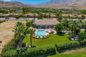 A residential area with a swimming pool surrounded by palm trees and a well-maintained lawn. - Putting Green, Saltwater Pool & Spa, 4 Fire Pits, Hammocks, Universal EV Charger (Palm Springs)