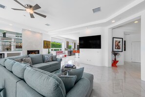 A spacious living area with a grey sectional sofa, a flat-screen TV mounted on the wall, and a ceiling fan. - Putting Green, Saltwater Pool & Spa, 4 Fire Pits, Hammocks, Universal EV Charger (Palm Springs)