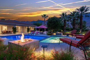 A pool area with lounge chairs, a fire pit, and a view of mountains at sunset. - Putting Green, Saltwater Pool & Spa, 4 Fire Pits, Hammocks, Universal EV Charger (Palm Springs)