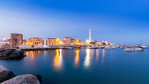 Un pueblo costero con un puerto tranquilo, edificios históricos y un faro destacado.