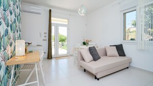 Una sala de estar moderna con un sofá, una mesa de comedor y una lámpara. Hay una puerta corredera de cristal que da a un jardín.